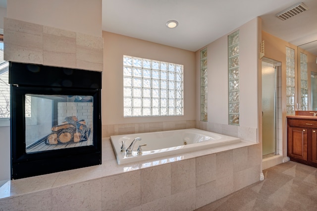 bathroom featuring visible vents, a shower stall, a garden tub, a tile fireplace, and vanity