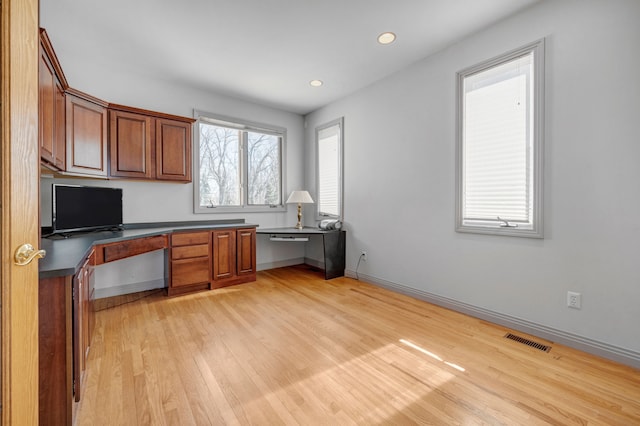 kitchen with light wood-type flooring, visible vents, brown cabinets, dark countertops, and built in study area