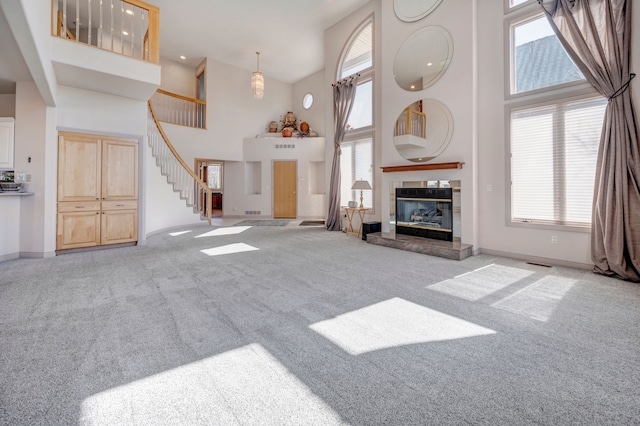 carpeted living area with stairway, plenty of natural light, a tile fireplace, and a towering ceiling