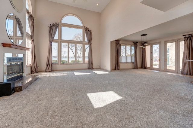 unfurnished living room featuring carpet flooring, baseboards, a high ceiling, and a fireplace