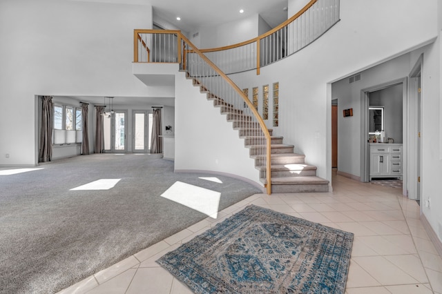 tiled entrance foyer featuring stairs, baseboards, a towering ceiling, and carpet flooring