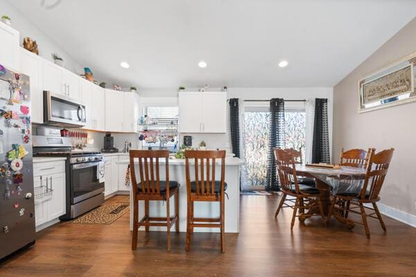 kitchen featuring dark wood finished floors, white cabinetry, stainless steel appliances, and a kitchen breakfast bar