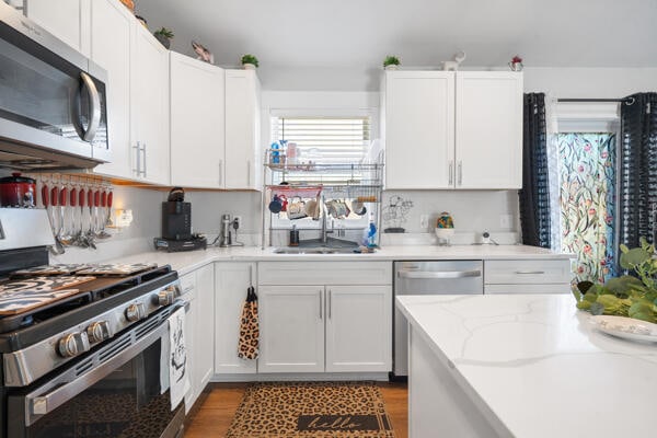 kitchen featuring white cabinetry, wood finished floors, appliances with stainless steel finishes, and a sink