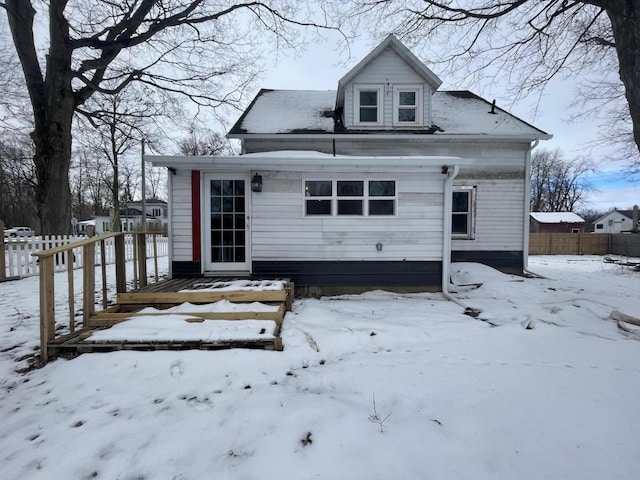 snow covered house with a wooden deck and fence