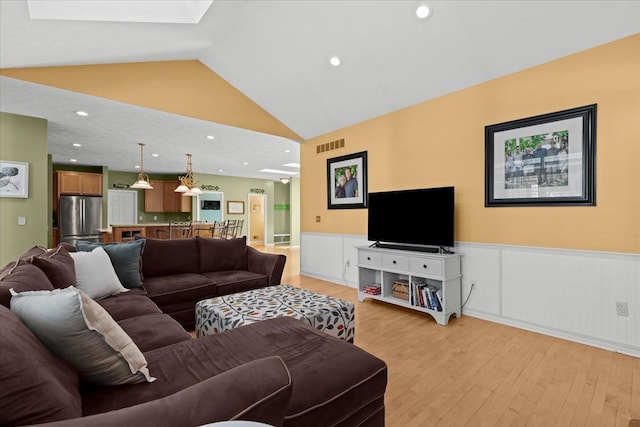 living room with a wainscoted wall, lofted ceiling with skylight, visible vents, recessed lighting, and light wood-style floors