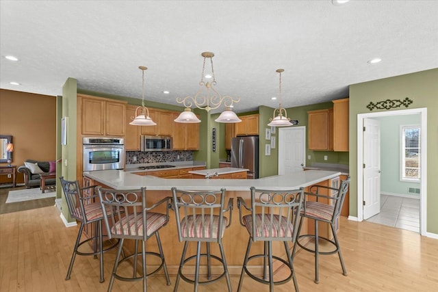 kitchen with a spacious island, light wood finished floors, stainless steel appliances, and tasteful backsplash