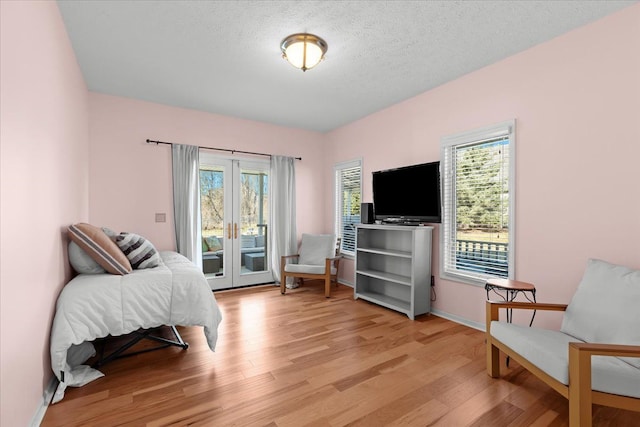 sitting room featuring french doors, baseboards, a textured ceiling, and light wood finished floors