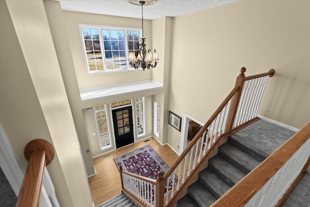 entryway featuring visible vents, a notable chandelier, wood finished floors, baseboards, and a towering ceiling