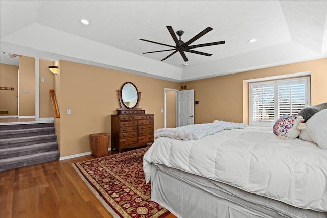 bedroom with wood finished floors, baseboards, recessed lighting, ceiling fan, and a raised ceiling