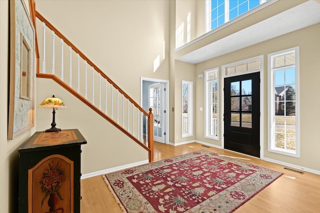 entryway with wood finished floors, visible vents, baseboards, a high ceiling, and stairs