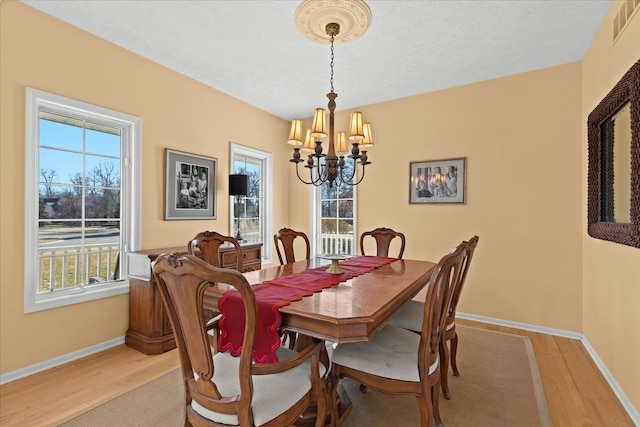 dining room with light wood finished floors, visible vents, baseboards, a notable chandelier, and a textured ceiling