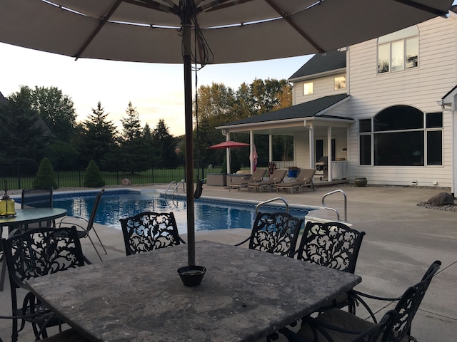 pool at dusk featuring outdoor dining area, a patio, a fenced in pool, and fence