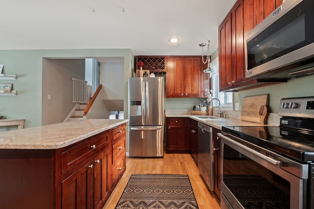 kitchen with a sink, light wood-type flooring, light stone countertops, and appliances with stainless steel finishes