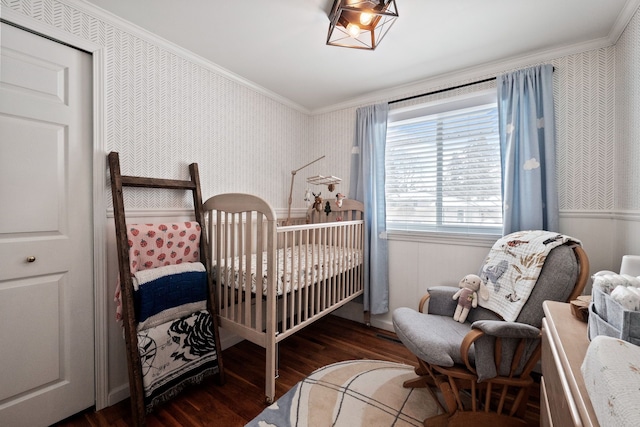 bedroom with a crib, wallpapered walls, crown molding, and wood finished floors