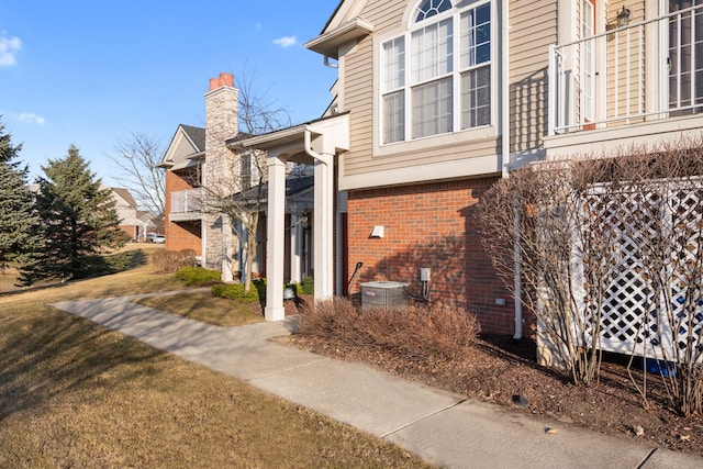 view of side of property featuring brick siding, cooling unit, a chimney, a balcony, and a yard