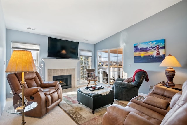 living area with visible vents, lofted ceiling, and a tiled fireplace