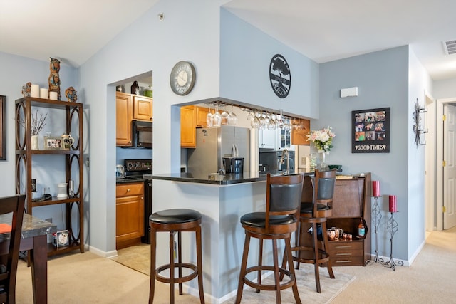 kitchen featuring black microwave, light colored carpet, a breakfast bar area, and stainless steel fridge with ice dispenser