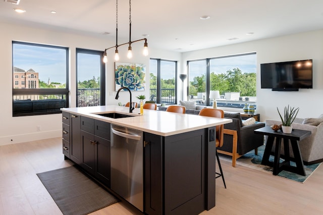 kitchen with light wood finished floors, a sink, light countertops, stainless steel dishwasher, and open floor plan