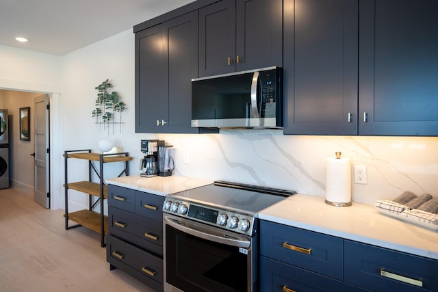 kitchen featuring stacked washer and dryer, decorative backsplash, light wood-style flooring, stainless steel appliances, and blue cabinets