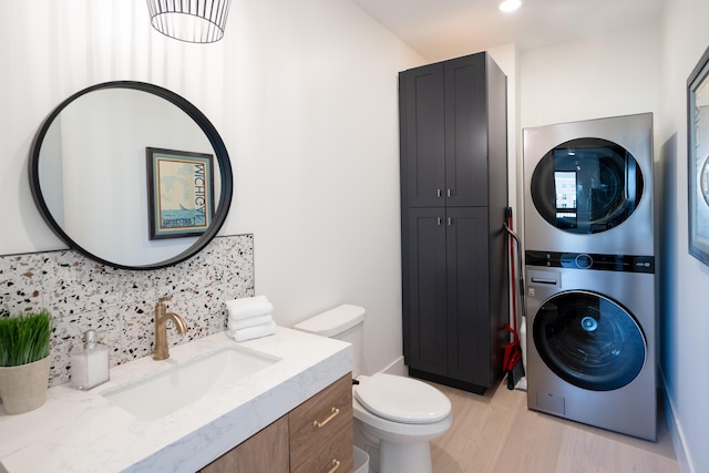 bathroom with toilet, decorative backsplash, wood finished floors, stacked washer / drying machine, and vanity