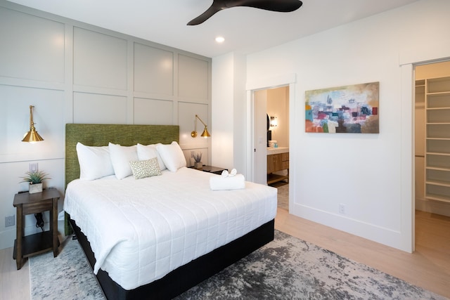 bedroom featuring a walk in closet, ensuite bath, recessed lighting, light wood-style floors, and a decorative wall