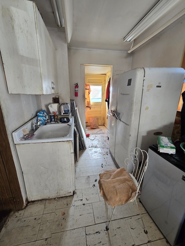 kitchen featuring light floors, light countertops, freestanding refrigerator, and a sink