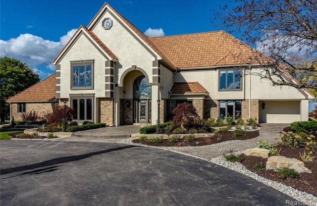 view of front of home featuring stucco siding, driveway, a tile roof, and a garage