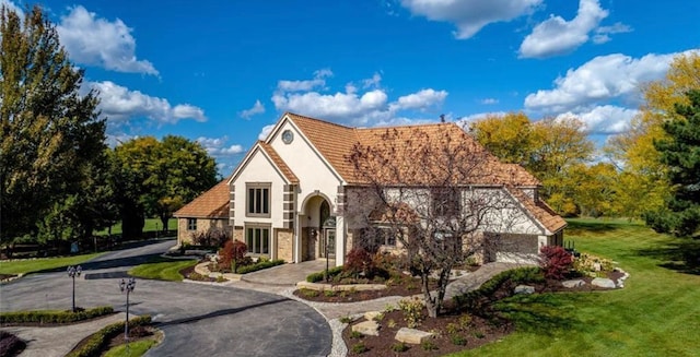 tudor home with stucco siding, stone siding, curved driveway, and a front yard