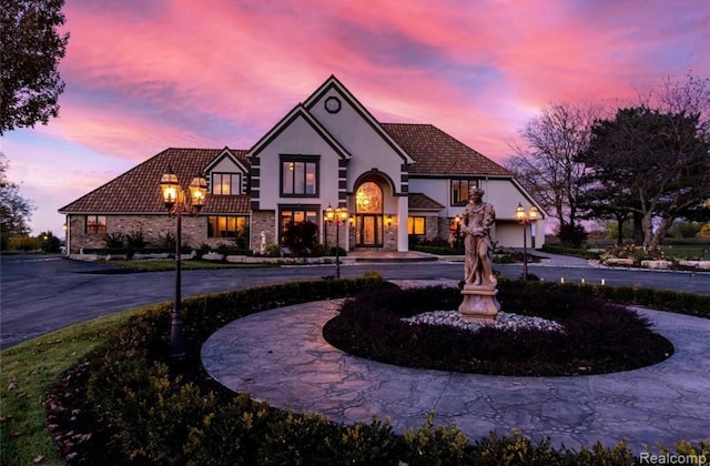 view of front of house with stucco siding, stone siding, curved driveway, and a tiled roof