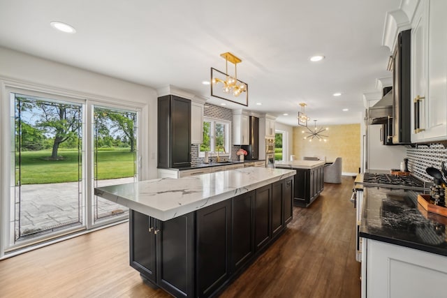 kitchen with a center island, light stone countertops, a chandelier, decorative backsplash, and wood finished floors