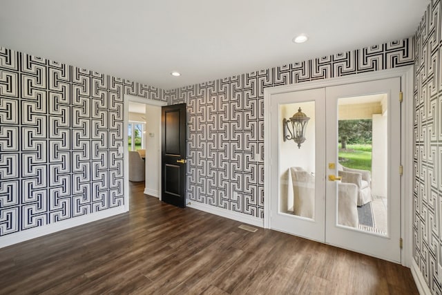 spare room featuring wallpapered walls, dark wood-style floors, french doors, and baseboards