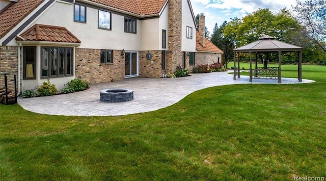 rear view of house featuring a fire pit, a gazebo, stucco siding, a lawn, and a patio