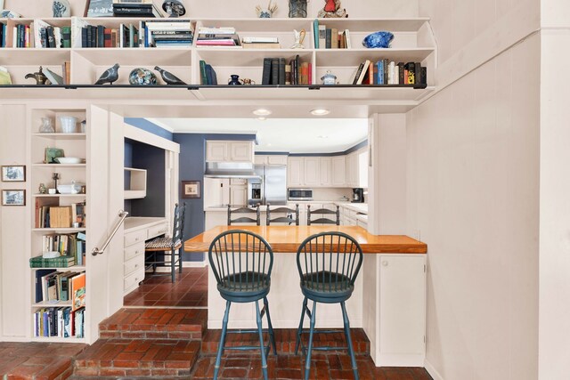 kitchen featuring a peninsula, baseboards, brick floor, and stainless steel appliances