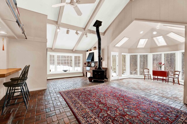 unfurnished living room with a ceiling fan, a wood stove, brick floor, beamed ceiling, and baseboard heating