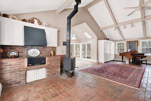 living room with beam ceiling, high vaulted ceiling, a ceiling fan, brick floor, and a wood stove