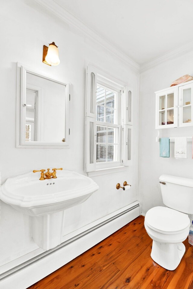 bathroom featuring toilet, wood finished floors, baseboard heating, and ornamental molding