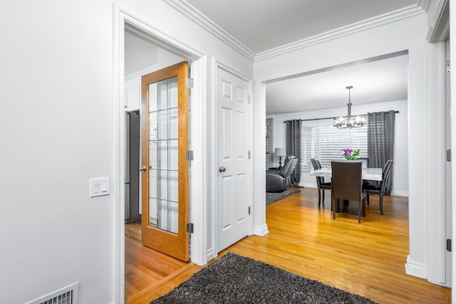 corridor with visible vents, baseboards, an inviting chandelier, light wood-style flooring, and crown molding