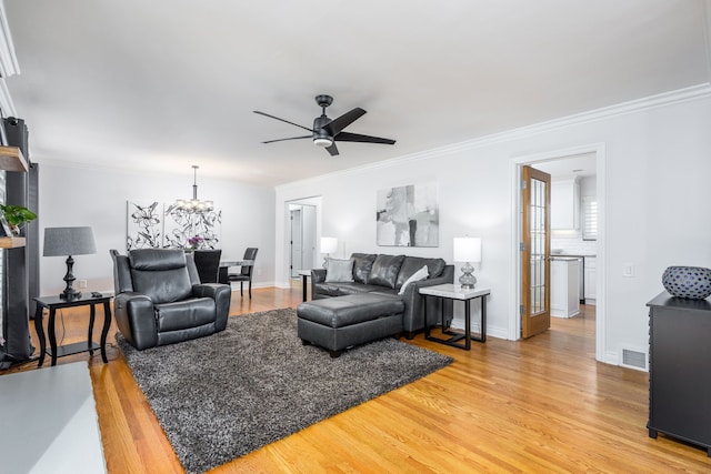 living room featuring visible vents, crown molding, baseboards, light wood-type flooring, and ceiling fan with notable chandelier