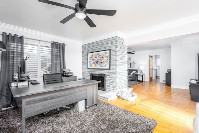 office space with crown molding, baseboards, a fireplace, wood finished floors, and a ceiling fan