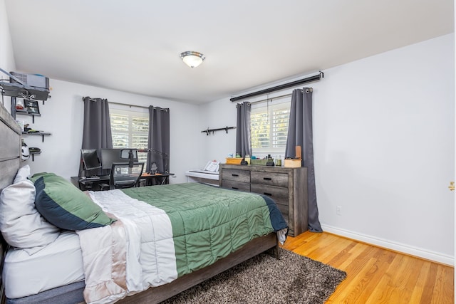 bedroom with multiple windows, wood finished floors, and baseboards