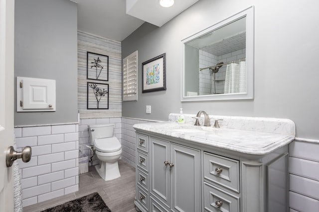 bathroom with toilet, a shower with shower curtain, tile walls, wainscoting, and vanity