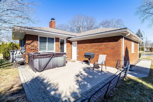 rear view of property with a patio, roof with shingles, brick siding, a chimney, and a hot tub