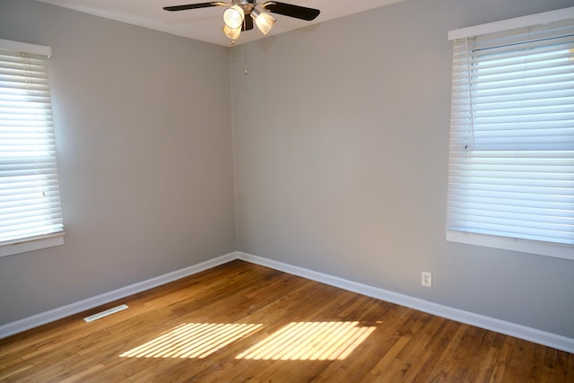 spare room featuring a ceiling fan, visible vents, wood finished floors, and baseboards