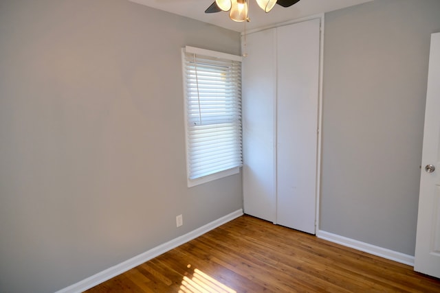 unfurnished bedroom featuring a closet, baseboards, wood finished floors, and a ceiling fan