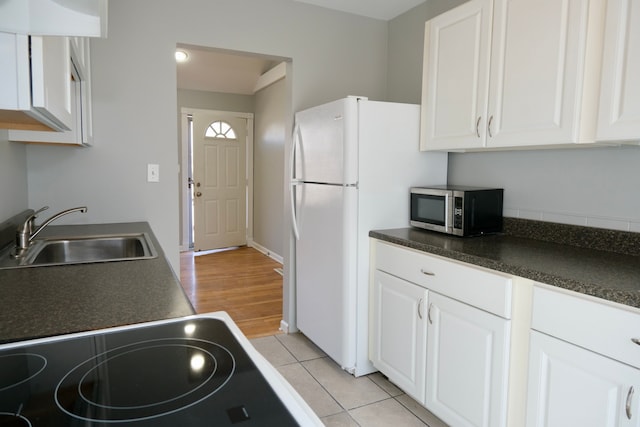 kitchen with a sink, stainless steel microwave, dark countertops, and white cabinetry