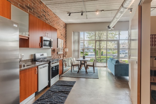 kitchen with brick wall, a sink, stainless steel appliances, rail lighting, and brown cabinets