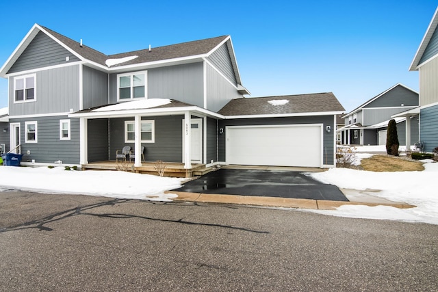 traditional home with a garage, a porch, a shingled roof, and aphalt driveway