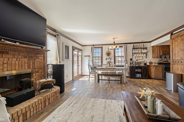 living area featuring wood finished floors, baseboards, an inviting chandelier, crown molding, and a brick fireplace