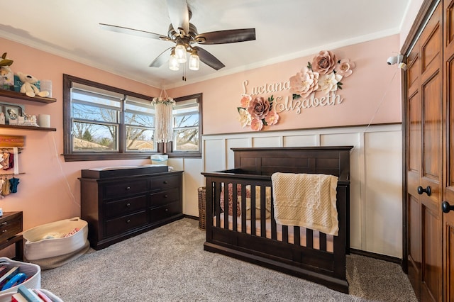 bedroom with light carpet, ornamental molding, a ceiling fan, wainscoting, and a decorative wall