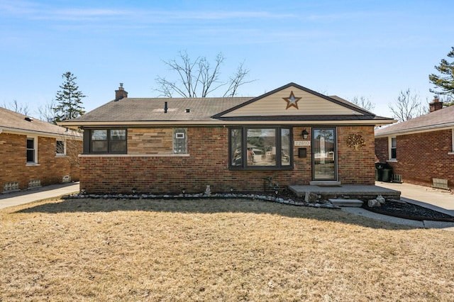 ranch-style house featuring a front yard, brick siding, a chimney, and a patio area